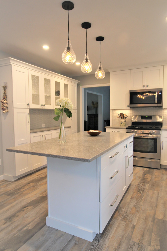 Photo of a medium sized nautical l-shaped kitchen/diner in Burlington with a submerged sink, shaker cabinets, white cabinets, engineered stone countertops, grey splashback, glass tiled splashback, stainless steel appliances, vinyl flooring, an island, multi-coloured floors and grey worktops.