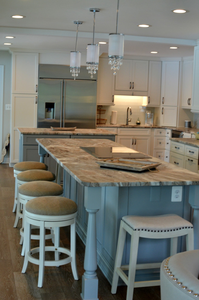 Inspiration for a mid-sized coastal l-shaped medium tone wood floor and brown floor open concept kitchen remodel in DC Metro with a farmhouse sink, shaker cabinets, white cabinets, granite countertops, white backsplash, glass tile backsplash, stainless steel appliances, an island and beige countertops