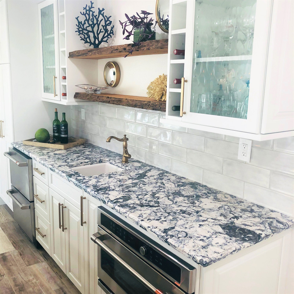 Example of a large beach style l-shaped porcelain tile and brown floor eat-in kitchen design in Miami with raised-panel cabinets, white cabinets, quartz countertops, white backsplash, ceramic backsplash, stainless steel appliances and multicolored countertops