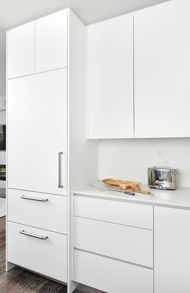 This is an example of a small modern u-shaped enclosed kitchen in Toronto with a submerged sink, flat-panel cabinets, white cabinets, engineered stone countertops, white splashback, marble splashback, stainless steel appliances, dark hardwood flooring, a breakfast bar, brown floors and white worktops.