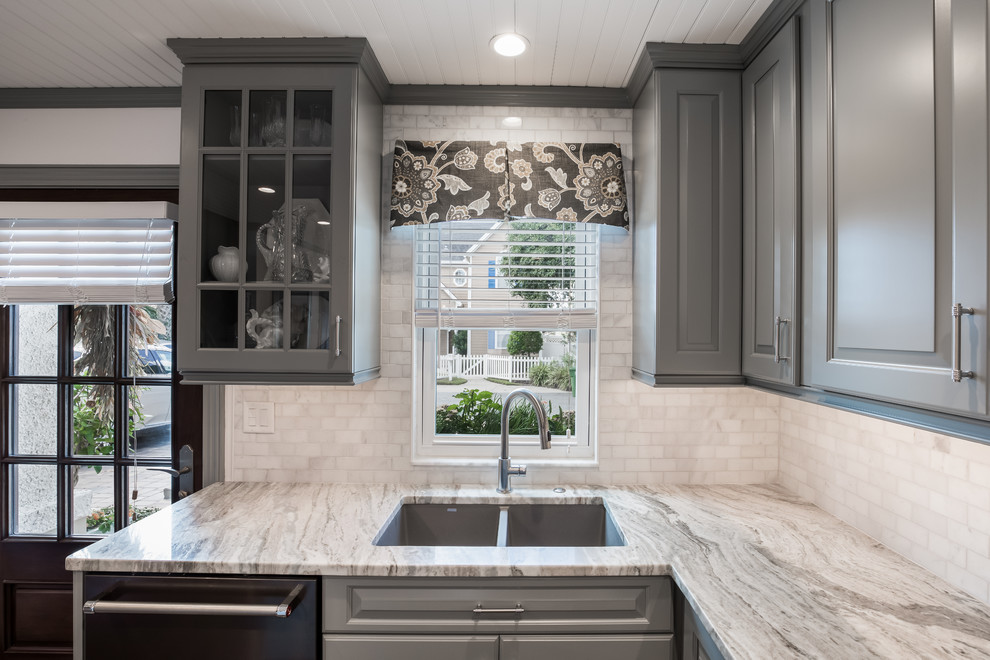 Bild på ett litet amerikanskt flerfärgad flerfärgat kök, med en undermonterad diskho, luckor med upphöjd panel, grå skåp, granitbänkskiva, vitt stänkskydd, stänkskydd i marmor, svarta vitvaror, vinylgolv, en köksö och brunt golv