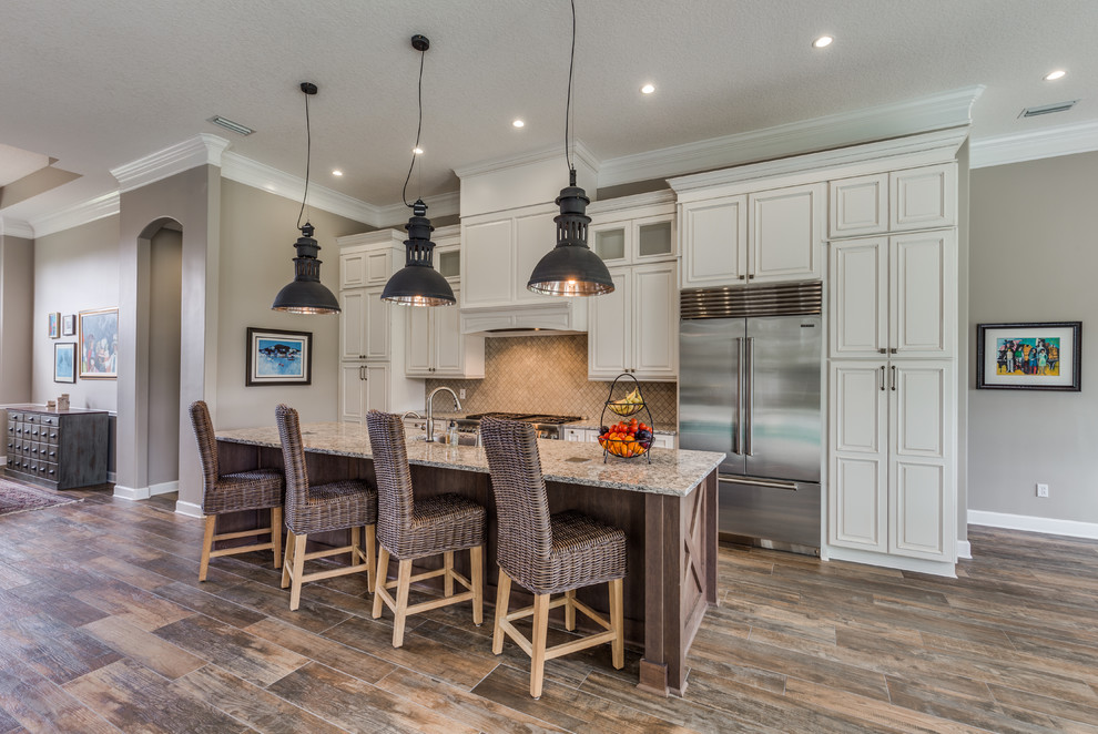 Beach style porcelain tile and brown floor kitchen photo in Jacksonville with raised-panel cabinets, beige cabinets, quartz countertops, marble backsplash, stainless steel appliances, an island, an undermount sink and beige backsplash