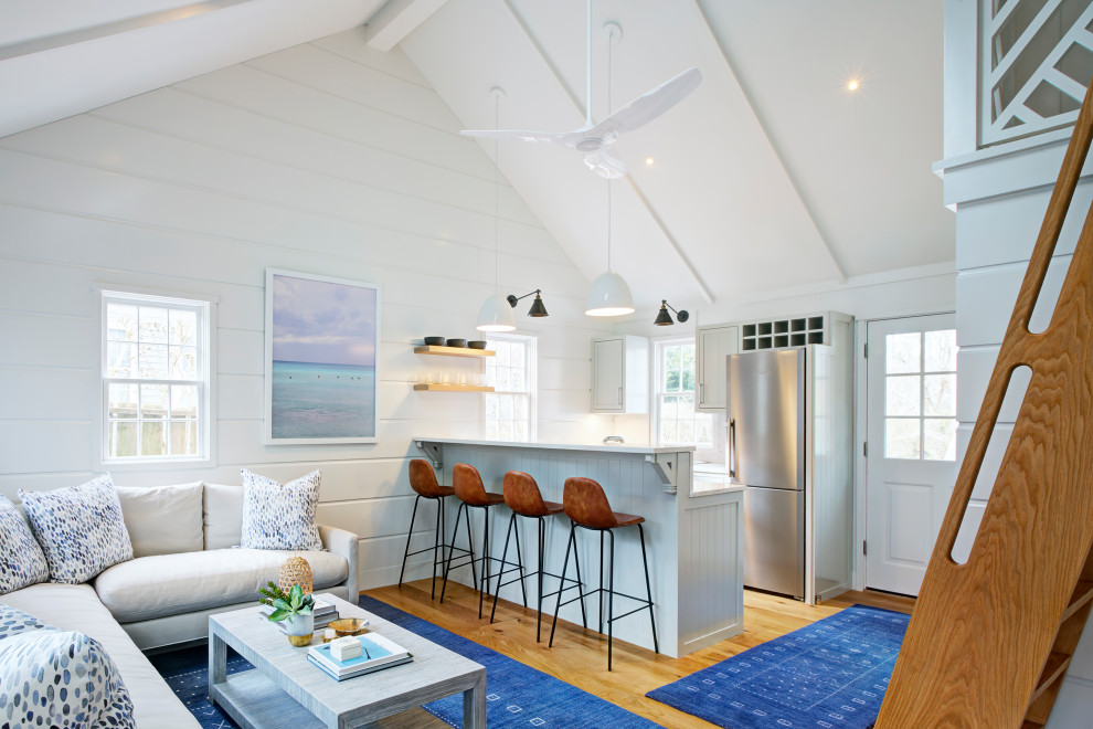 Cette image montre une cuisine ouverte parallèle marine avec des portes de placard bleues, un électroménager en acier inoxydable, parquet clair, une péninsule et un plan de travail blanc.