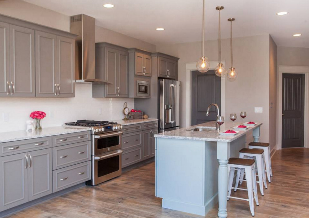 Example of a mid-sized beach style u-shaped medium tone wood floor eat-in kitchen design in Grand Rapids with an undermount sink, shaker cabinets, gray cabinets, quartzite countertops, white backsplash, subway tile backsplash, stainless steel appliances and an island