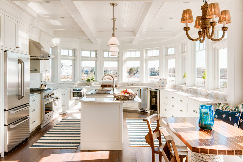 Maritime Wohnküche mit Doppelwaschbecken, Schrankfronten mit vertiefter Füllung, weißen Schränken, Küchenrückwand in Weiß, Rückwand aus Metrofliesen, Küchengeräten aus Edelstahl, braunem Holzboden und Kücheninsel in Portland Maine