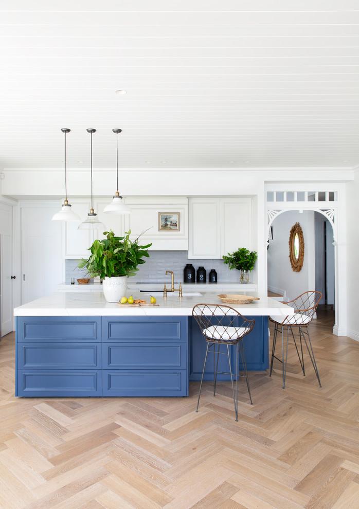 Exemple d'une cuisine ouverte bicolore chic avec un évier de ferme, un placard avec porte à panneau encastré, des portes de placard blanches, une crédence bleue, parquet clair, îlot, un sol beige et un plan de travail blanc.