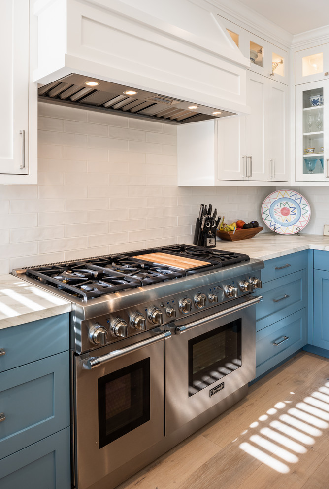サンフランシスコにある高級な広いトランジショナルスタイルのおしゃれなキッチン (アンダーカウンターシンク、シェーカースタイル扉のキャビネット、青いキャビネット、大理石カウンター、メタリックのキッチンパネル、ミラータイルのキッチンパネル、パネルと同色の調理設備、淡色無垢フローリング、茶色い床、グレーのキッチンカウンター) の写真