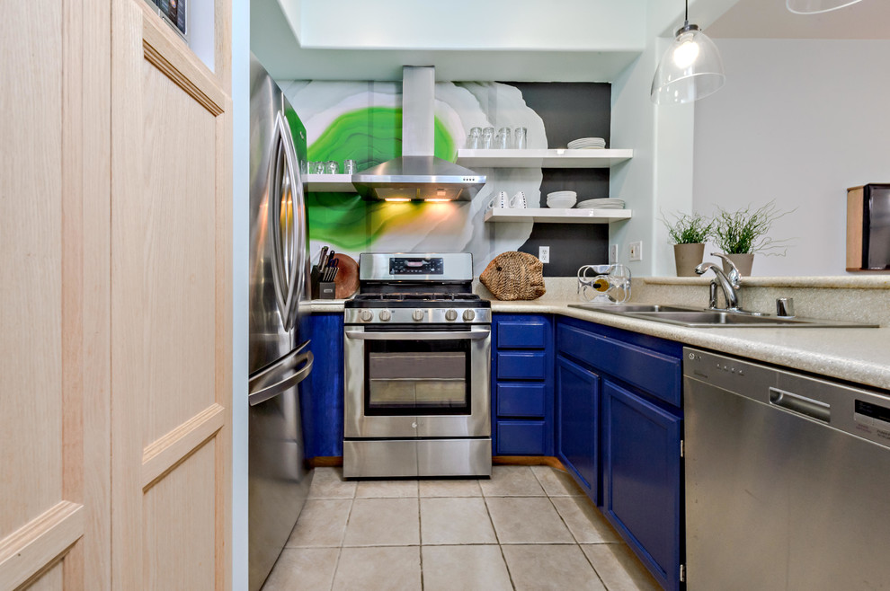 Cette image montre une cuisine design en U avec un évier 2 bacs, des portes de placard bleues, un électroménager en acier inoxydable et papier peint.
