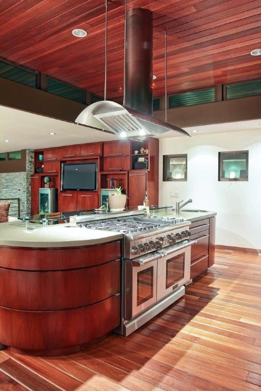 Inspiration for a large coastal single-wall medium tone wood floor eat-in kitchen remodel in Los Angeles with a single-bowl sink, flat-panel cabinets, medium tone wood cabinets, concrete countertops, white backsplash, glass tile backsplash, stainless steel appliances and an island
