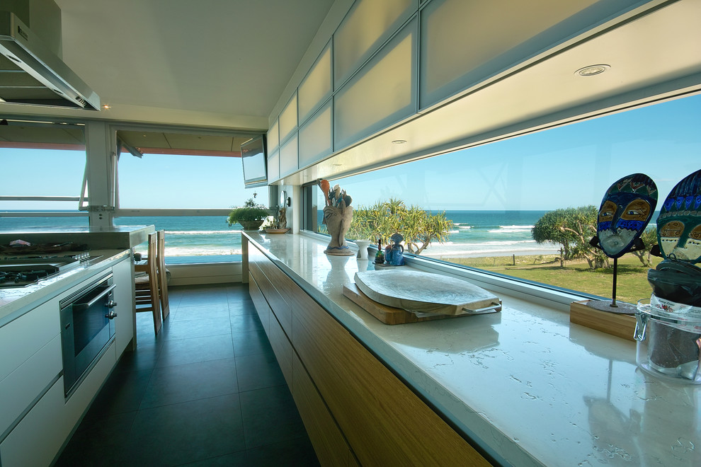 На фото: параллельная кухня в морском стиле с обеденным столом, врезной мойкой, стеклянными фасадами и светлыми деревянными фасадами