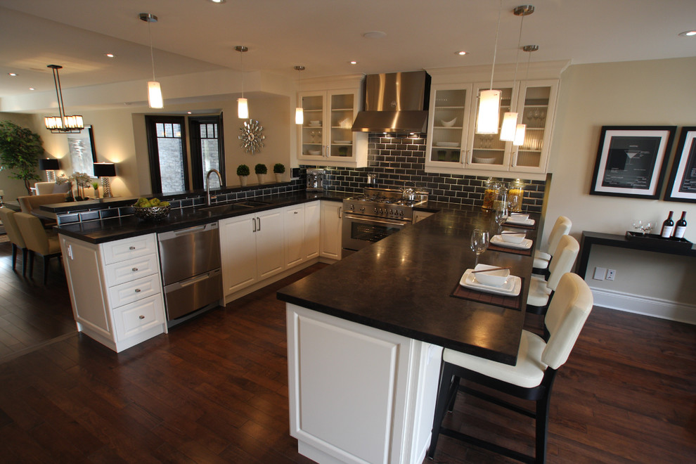 Large transitional u-shaped dark wood floor open concept kitchen photo in Toronto with an undermount sink, white cabinets, granite countertops, metallic backsplash, subway tile backsplash, stainless steel appliances, raised-panel cabinets and a peninsula