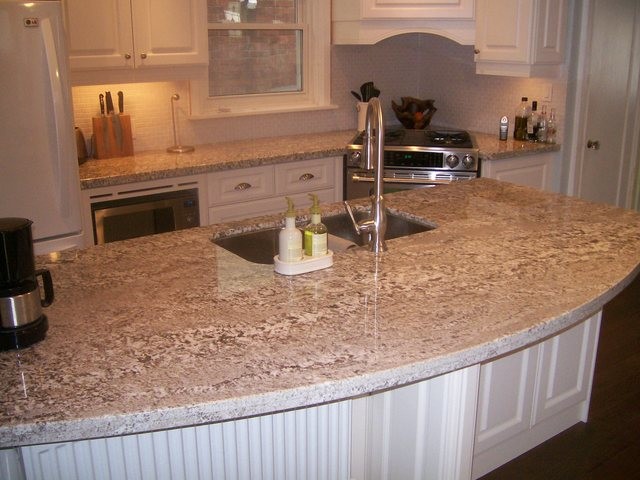Inredning av ett klassiskt kök, med en dubbel diskho, luckor med infälld panel, vita skåp, granitbänkskiva, vitt stänkskydd, stänkskydd i keramik, rostfria vitvaror, ljust trägolv och en halv köksö