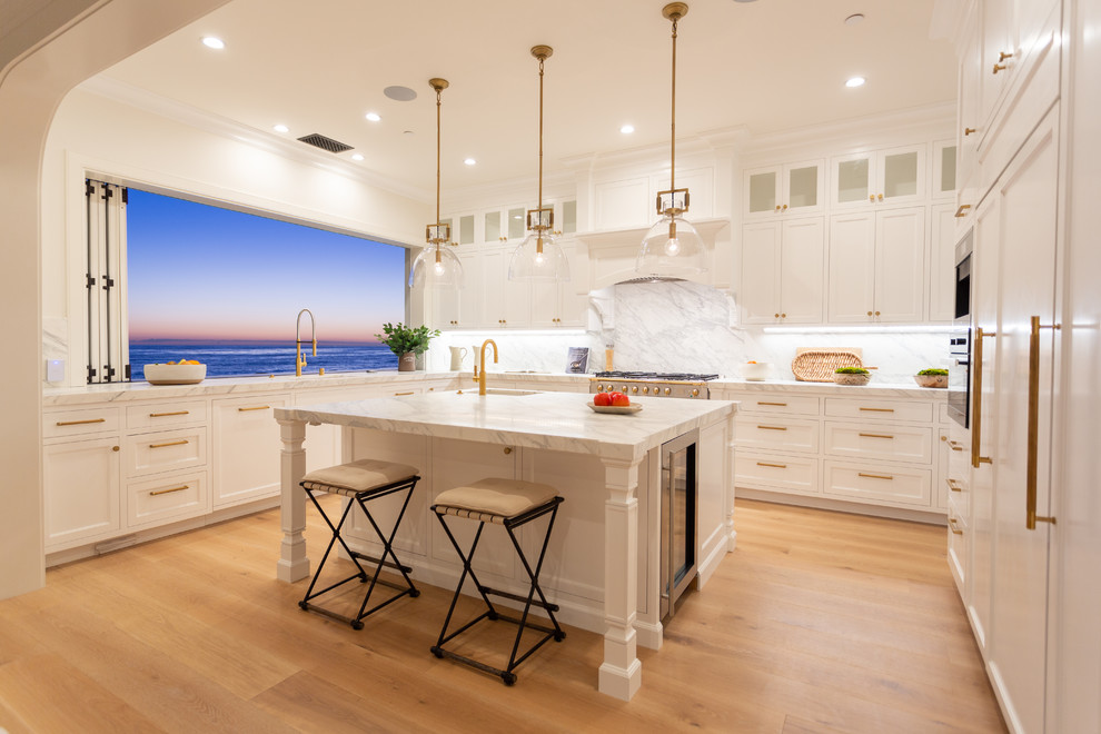 Foto på ett maritimt vit u-kök, med en undermonterad diskho, skåp i shakerstil, vita skåp, vitt stänkskydd, stänkskydd i sten, integrerade vitvaror, mellanmörkt trägolv, en köksö och brunt golv