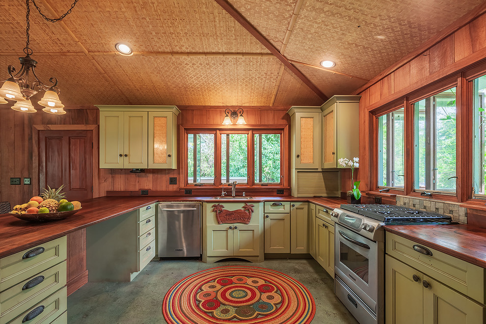 Exotisk inredning av ett kök, med en enkel diskho, luckor med infälld panel, gröna skåp, träbänkskiva, rostfria vitvaror och betonggolv