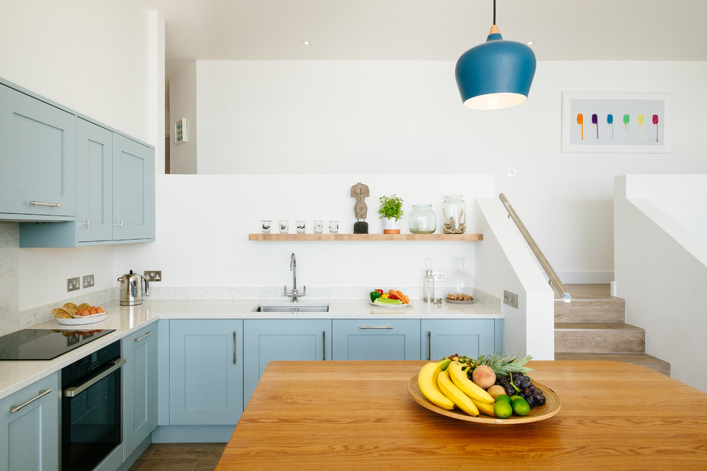 Maritime Küche in L-Form mit Unterbauwaschbecken, Schrankfronten im Shaker-Stil, blauen Schränken, Küchenrückwand in Weiß, schwarzen Elektrogeräten, Kücheninsel und weißer Arbeitsplatte in Cornwall