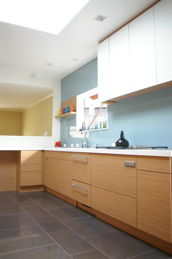 Идея дизайна: кухня в стиле модернизм с плоскими фасадами, светлыми деревянными фасадами, синим фартуком и фартуком из стекла