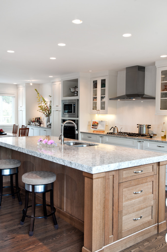 Medium sized classic galley open plan kitchen in Vancouver with a submerged sink, shaker cabinets, white cabinets, engineered stone countertops, white splashback, porcelain splashback, stainless steel appliances, dark hardwood flooring and an island.