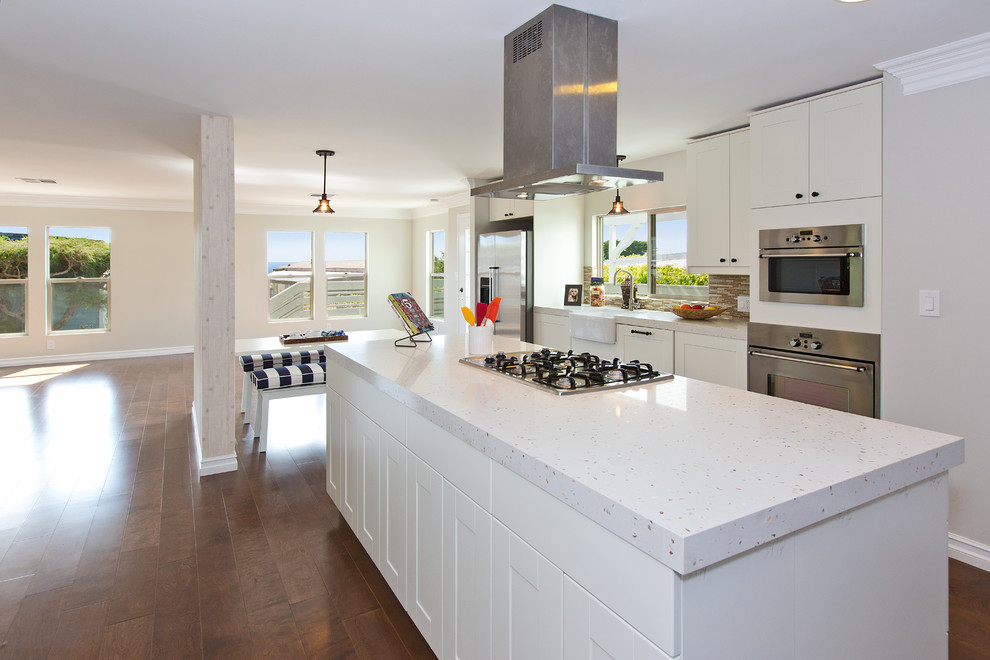 Modelo de cocina lineal costera de tamaño medio abierta con puertas de armario blancas, salpicadero beige, electrodomésticos de acero inoxidable y una isla
