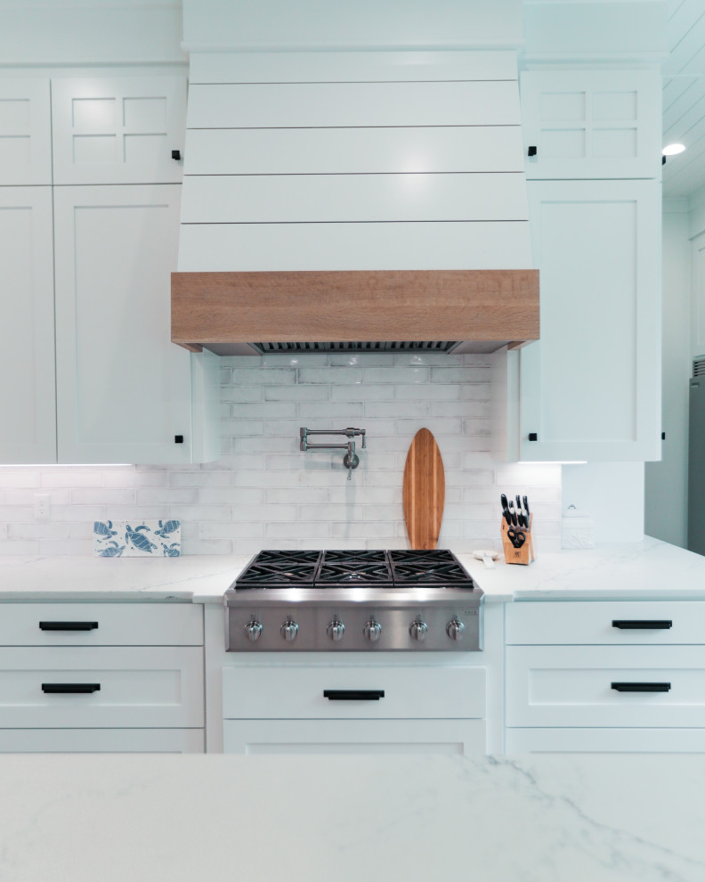 This is an example of a large coastal l-shaped kitchen in Other with a belfast sink, white cabinets, granite worktops, multi-coloured splashback, ceramic splashback, stainless steel appliances, light hardwood flooring, an island, multicoloured worktops and a timber clad ceiling.