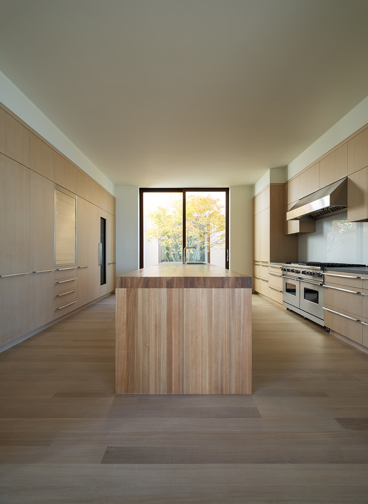 Cette photo montre une cuisine parallèle et encastrable moderne en bois clair fermée avec un placard à porte plane, une crédence blanche, parquet clair, îlot, un sol beige et un plan de travail beige.