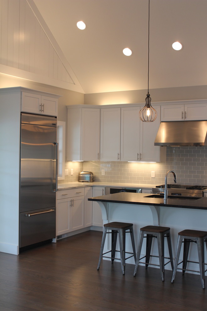 Mid-sized beach style l-shaped medium tone wood floor and brown floor open concept kitchen photo in Chicago with an undermount sink, recessed-panel cabinets, white cabinets, granite countertops, gray backsplash, ceramic backsplash, stainless steel appliances and an island