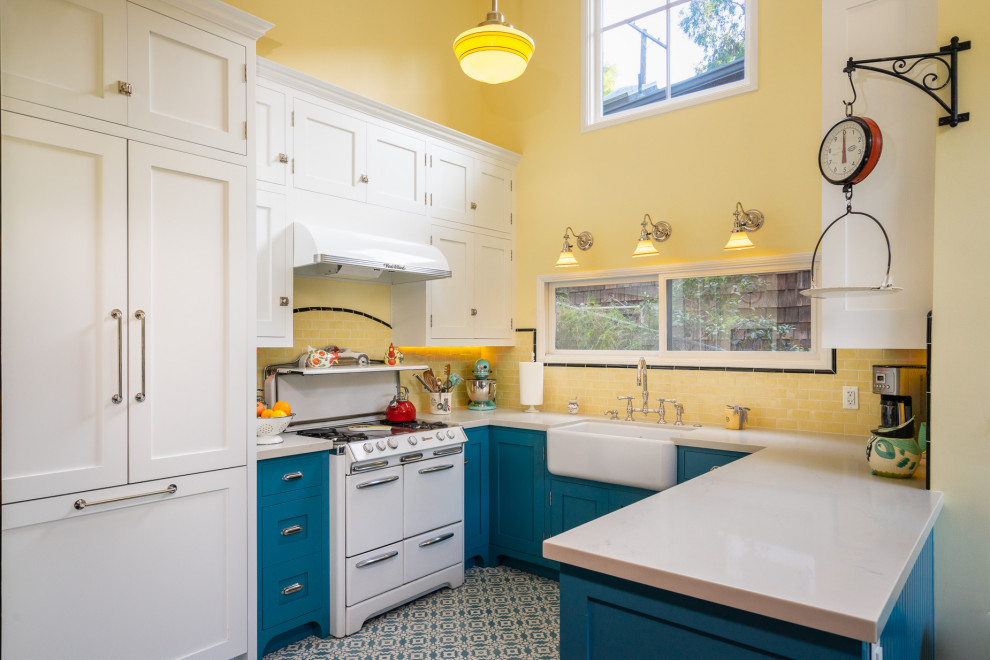 Inredning av ett lantligt litet vit vitt kök, med en rustik diskho, luckor med profilerade fronter, blå skåp, bänkskiva i kvarts, gult stänkskydd, stänkskydd i tunnelbanekakel, vita vitvaror, cementgolv och blått golv