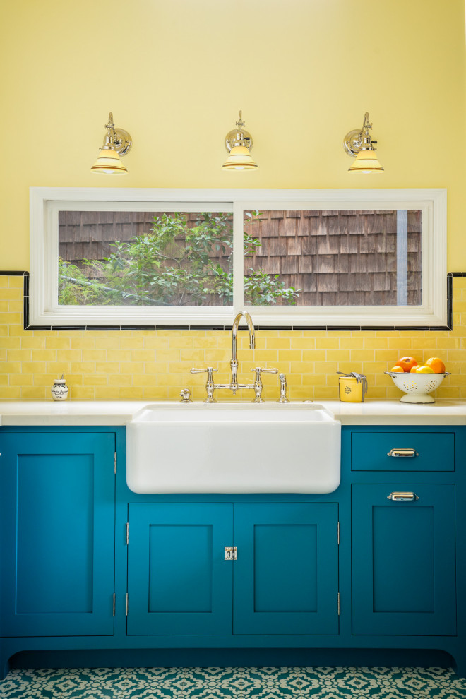 Пример оригинального дизайна: маленькая п-образная кухня в стиле кантри с обеденным столом, с полувстраиваемой мойкой (с передним бортиком), фасадами с декоративным кантом, синими фасадами, столешницей из кварцевого агломерата, желтым фартуком, фартуком из плитки кабанчик, белой техникой, полом из цементной плитки, синим полом и белой столешницей для на участке и в саду