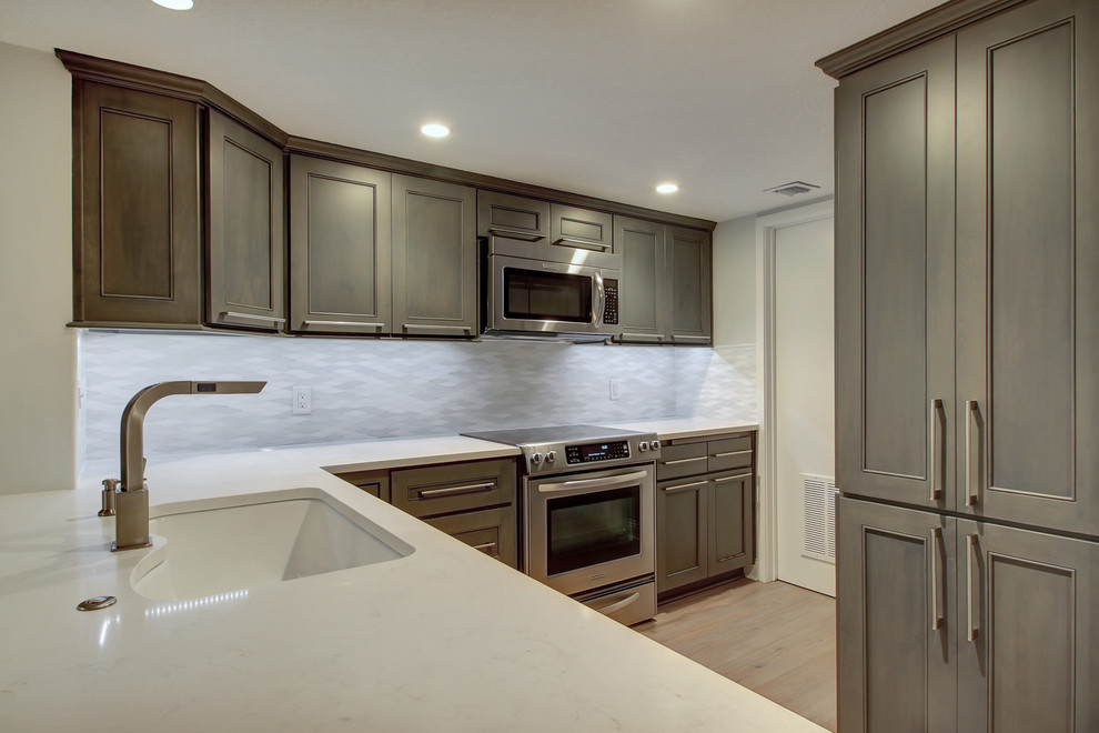 Example of a small trendy l-shaped light wood floor kitchen pantry design in Jacksonville with an undermount sink, shaker cabinets, gray cabinets, gray backsplash, stainless steel appliances, no island, quartz countertops and glass tile backsplash