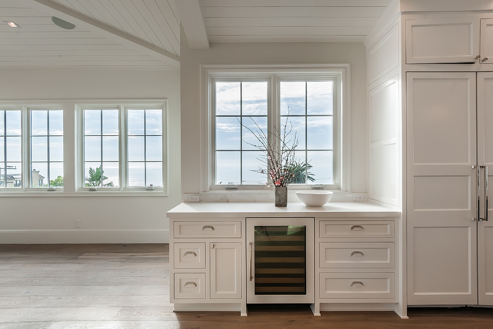 Idéer för stora maritima linjära kök med öppen planlösning, med luckor med infälld panel, marmorbänkskiva, vitt stänkskydd, stänkskydd i marmor, integrerade vitvaror, en köksö och vita skåp
