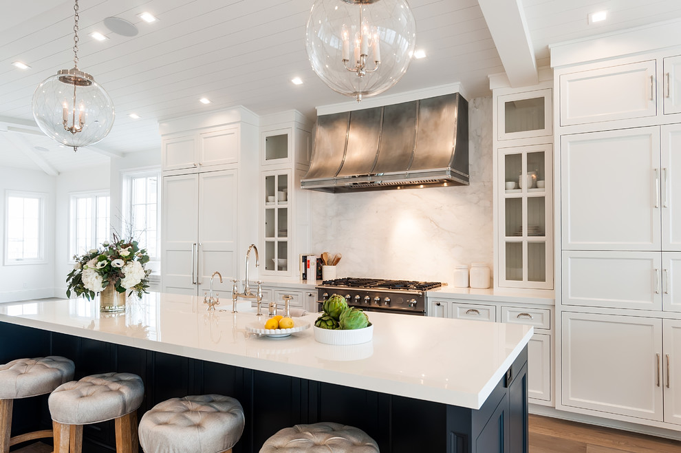 Inspiration for a large coastal galley open plan kitchen in San Diego with recessed-panel cabinets, white cabinets, composite countertops, white splashback, marble splashback, stainless steel appliances, light hardwood flooring and an island.