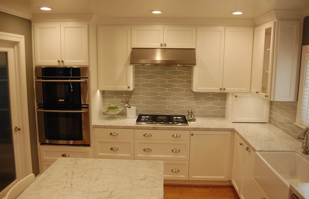 Inspiration for a mid-sized timeless l-shaped medium tone wood floor eat-in kitchen remodel in San Francisco with a farmhouse sink, shaker cabinets, white cabinets, marble countertops, green backsplash, subway tile backsplash, stainless steel appliances and an island