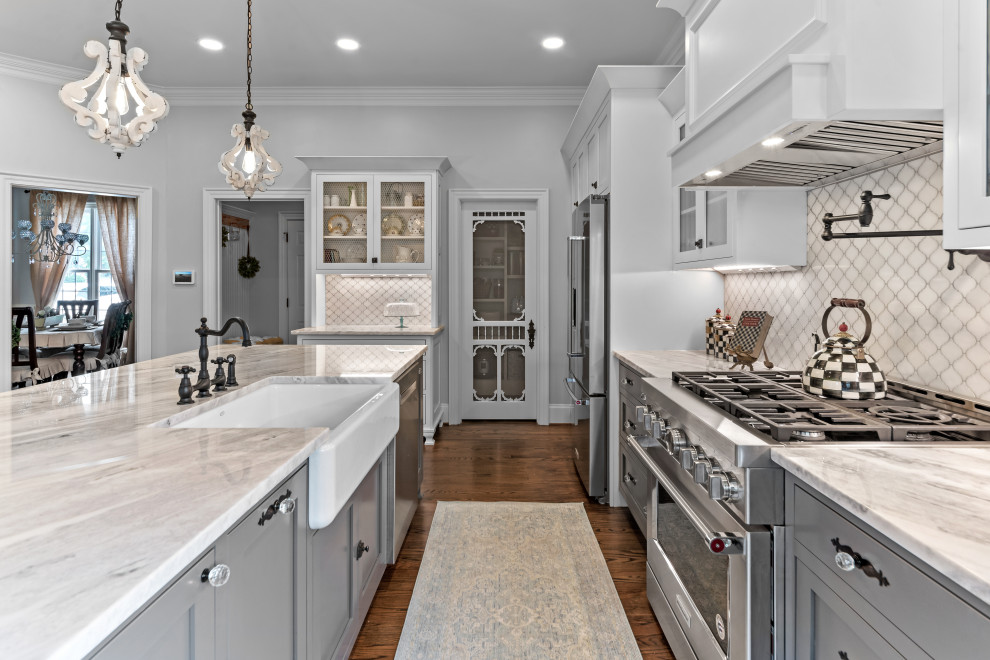Inspiration for a large shabby-chic style l-shaped dark wood floor and brown floor open concept kitchen remodel in Raleigh with a farmhouse sink, shaker cabinets, white cabinets, marble countertops, white backsplash, marble backsplash, stainless steel appliances, an island and multicolored countertops