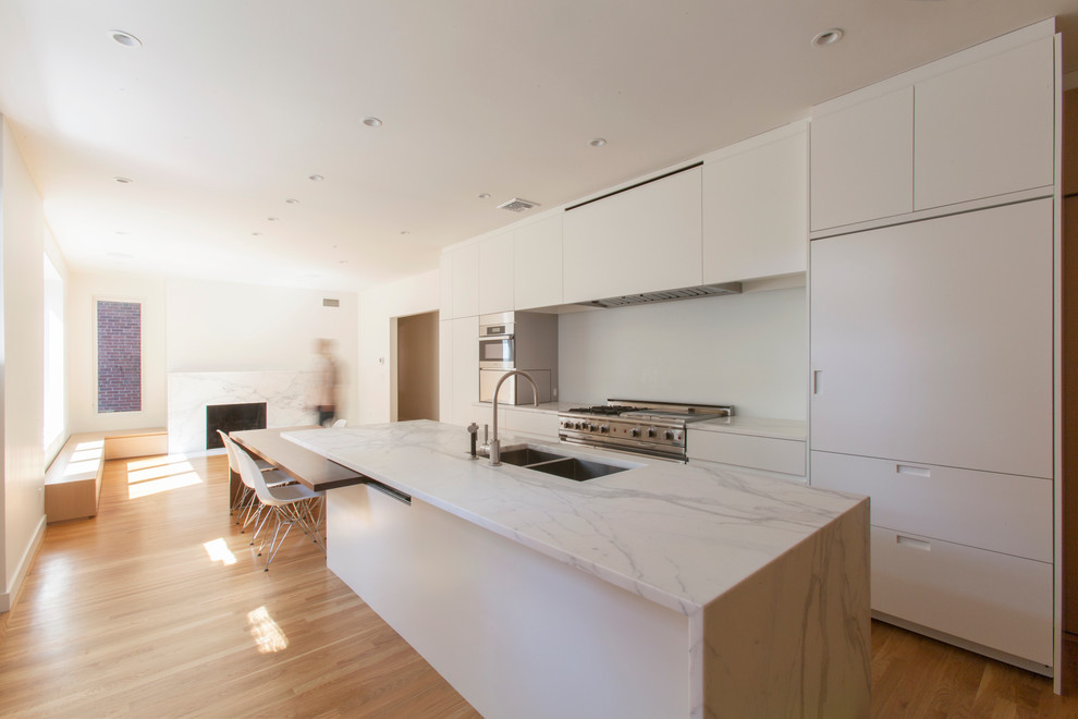 Minimalist single-wall light wood floor eat-in kitchen photo in Boston with an island, an undermount sink, flat-panel cabinets, white cabinets, marble countertops, white backsplash and stainless steel appliances
