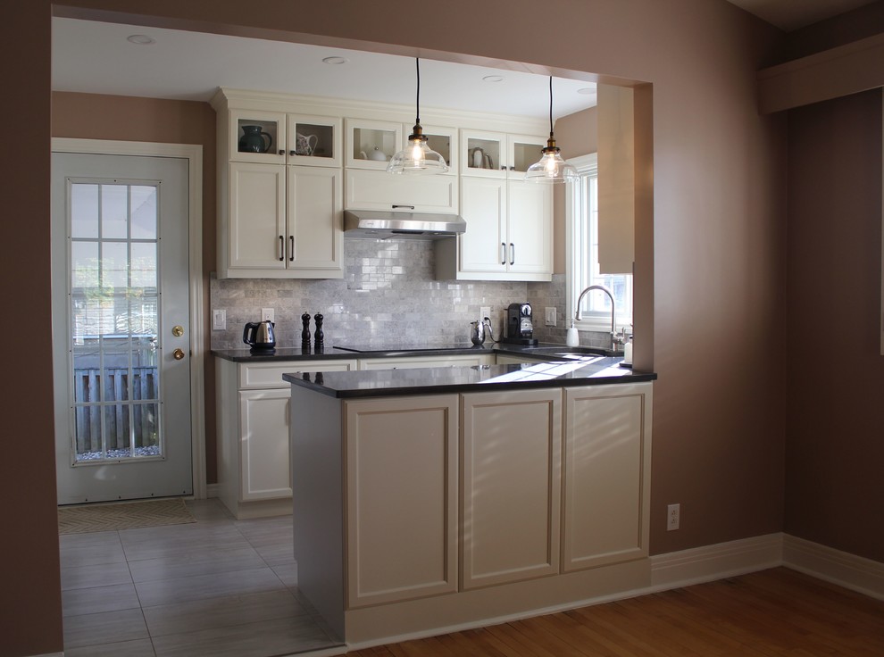 Photo of a small traditional u-shaped kitchen in Montreal with a submerged sink, recessed-panel cabinets, beige cabinets, engineered stone countertops, grey splashback, stone tiled splashback, stainless steel appliances, ceramic flooring, a breakfast bar, grey floors and grey worktops.