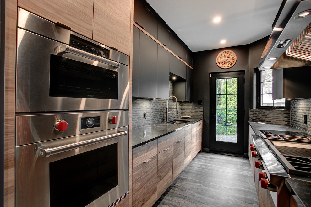 Zweizeilige Moderne Küche mit Unterbauwaschbecken, flächenbündigen Schrankfronten, dunklen Holzschränken, Küchenrückwand in Grau, Küchengeräten aus Edelstahl, dunklem Holzboden, braunem Boden und schwarzer Arbeitsplatte in Montreal