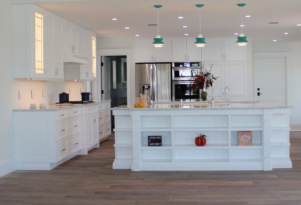 This is an example of a large nautical single-wall open plan kitchen in Miami with white cabinets, engineered stone countertops, white splashback, stainless steel appliances, multiple islands, shaker cabinets and laminate floors.