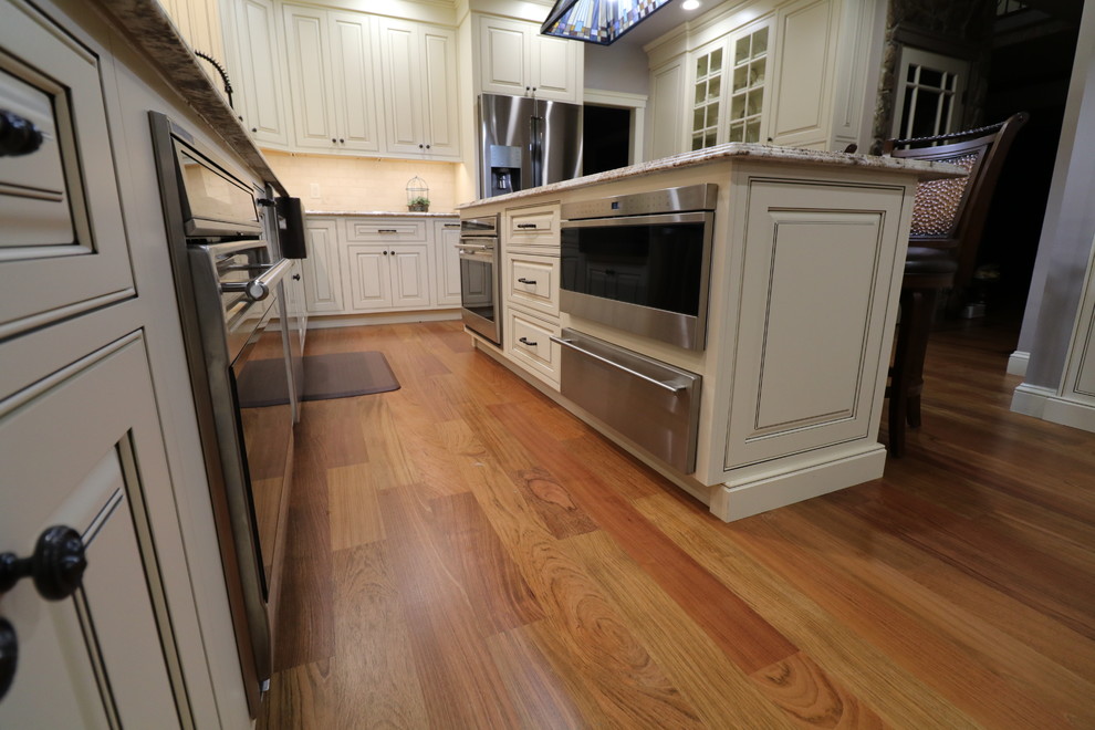 Mid-sized tuscan l-shaped medium tone wood floor and brown floor open concept kitchen photo in Boston with a farmhouse sink, beaded inset cabinets, beige cabinets, granite countertops, beige backsplash, subway tile backsplash, stainless steel appliances, an island and multicolored countertops