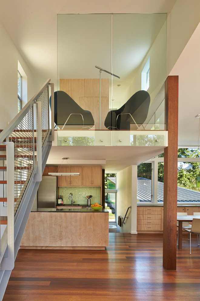 Offene Moderne Küche in U-Form mit flächenbündigen Schrankfronten, hellen Holzschränken, Küchenrückwand in Grün, Küchengeräten aus Edelstahl, dunklem Holzboden und Halbinsel in Seattle