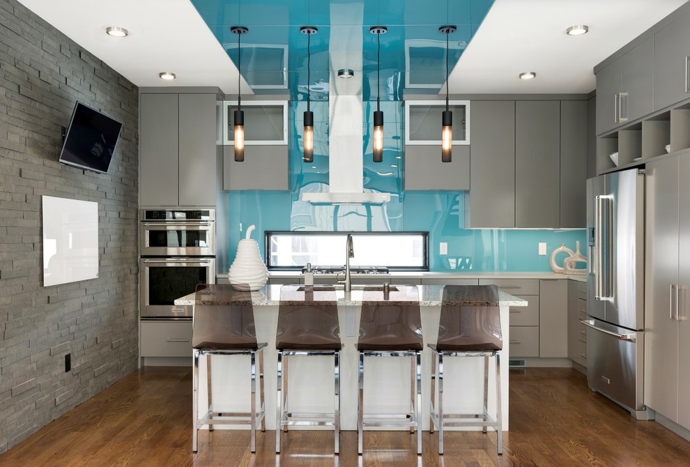 Inredning av ett modernt grå grått l-kök, med en undermonterad diskho, släta luckor, grå skåp, blått stänkskydd, glaspanel som stänkskydd, rostfria vitvaror, mellanmörkt trägolv och en köksö