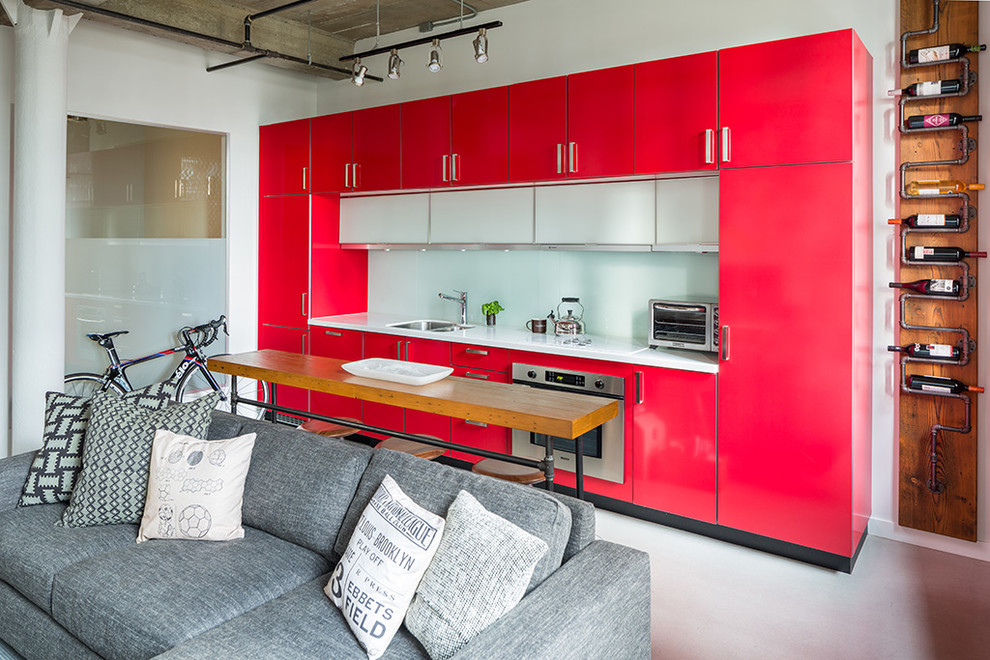 Design ideas for a small industrial galley open plan kitchen in Vancouver with a double-bowl sink, flat-panel cabinets, red cabinets, glass sheet splashback, stainless steel appliances, concrete flooring, an island, quartz worktops and white splashback.