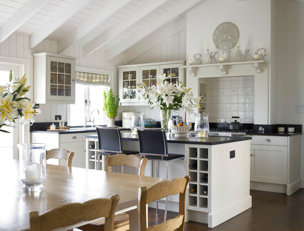 Mittelgroße Landhaus Wohnküche in L-Form mit Landhausspüle, Schrankfronten im Shaker-Stil, weißen Schränken, Granit-Arbeitsplatte, dunklem Holzboden, Kücheninsel, Küchenrückwand in Weiß und Rückwand aus Keramikfliesen in Wiltshire