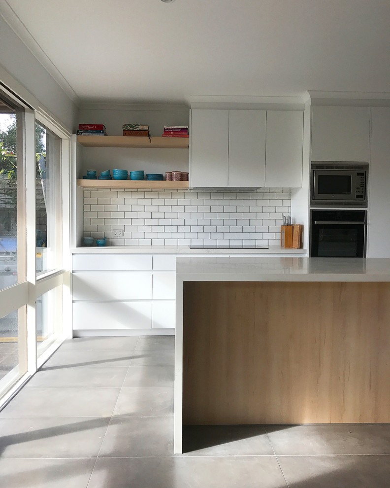 Mid-sized minimalist galley slate floor and gray floor kitchen pantry photo in Melbourne with an undermount sink, flat-panel cabinets, white cabinets, quartz countertops, white backsplash, porcelain backsplash, black appliances and an island