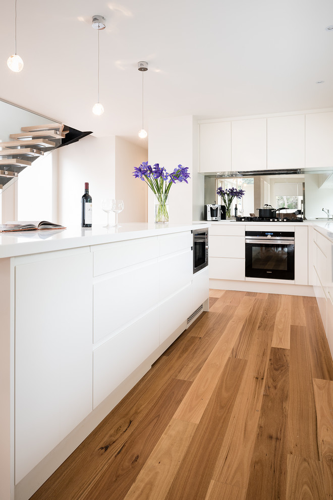Exempel på ett mellanstort modernt vit vitt kök, med en integrerad diskho, släta luckor, vita skåp, bänkskiva i koppar, spegel som stänkskydd, rostfria vitvaror, mellanmörkt trägolv, en köksö och stänkskydd med metallisk yta