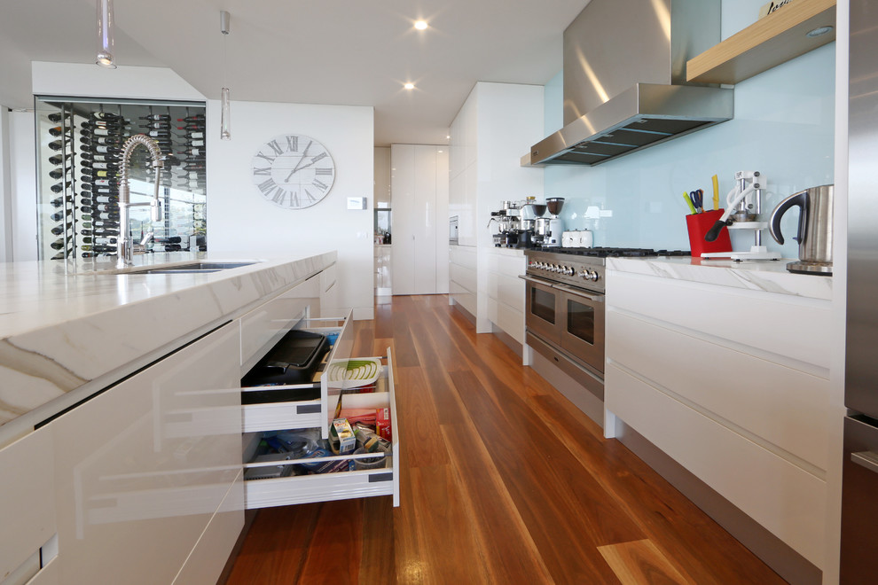 Example of a trendy galley kitchen design in Melbourne with an undermount sink, flat-panel cabinets, white cabinets, blue backsplash, glass sheet backsplash and stainless steel appliances