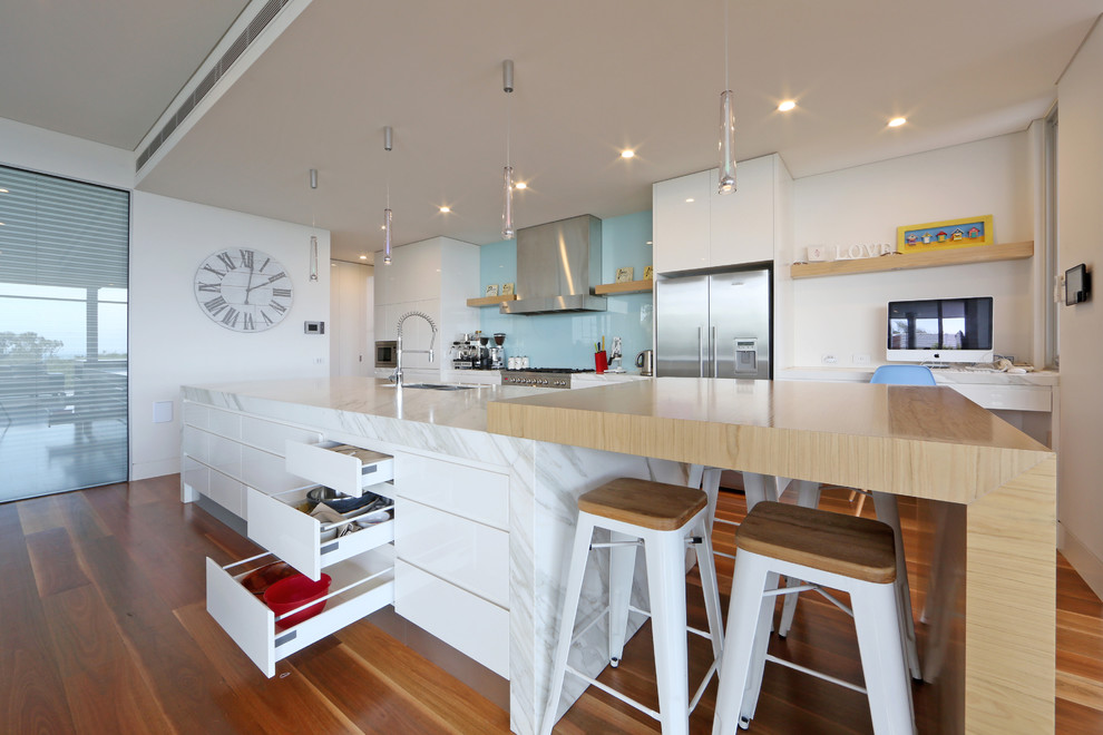 Inspiration for a contemporary galley kitchen in Melbourne with a submerged sink, flat-panel cabinets, white cabinets, wood worktops, blue splashback, glass sheet splashback and stainless steel appliances.