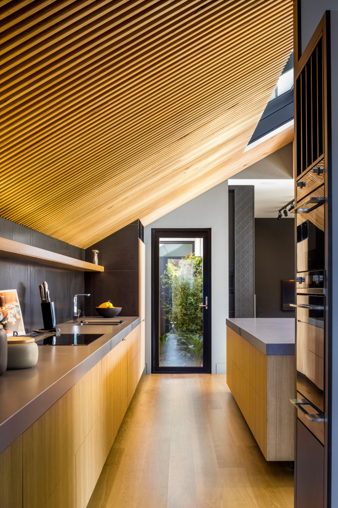Inspiration pour une cuisine ouverte parallèle minimaliste en bois clair de taille moyenne avec un placard avec porte à panneau encastré, un plan de travail en surface solide, parquet clair, îlot, un sol marron et un plan de travail gris.