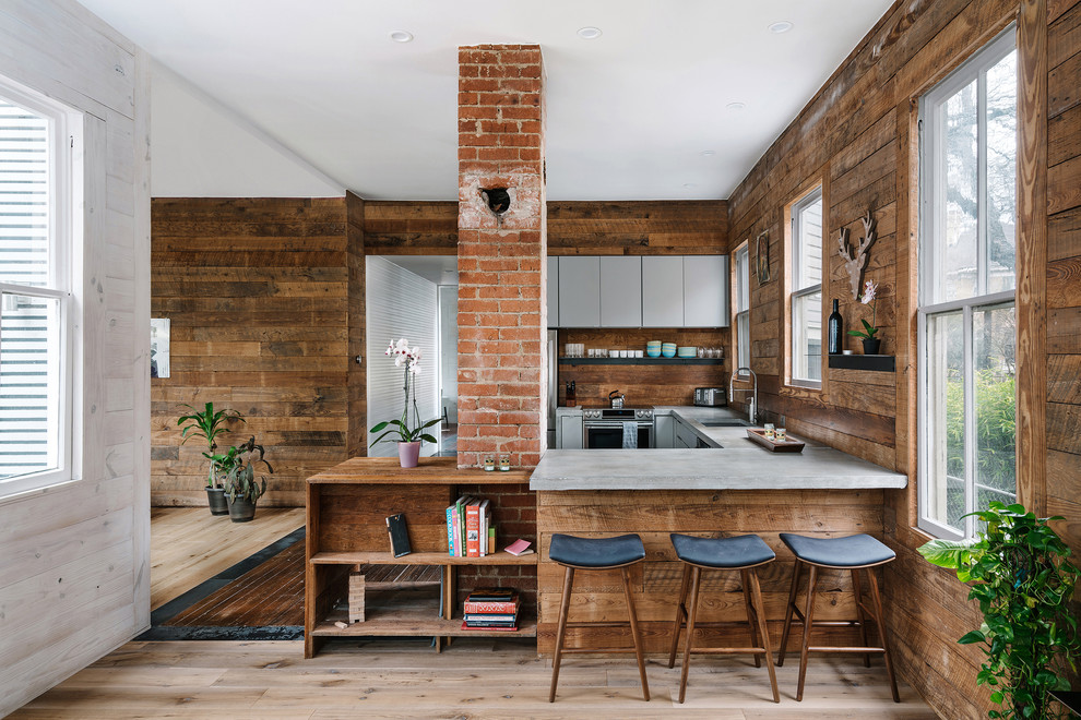 Bild på ett rustikt grå grått u-kök, med en undermonterad diskho, släta luckor, grå skåp, bänkskiva i betong, brunt stänkskydd, stänkskydd i trä, rostfria vitvaror, ljust trägolv och en halv köksö