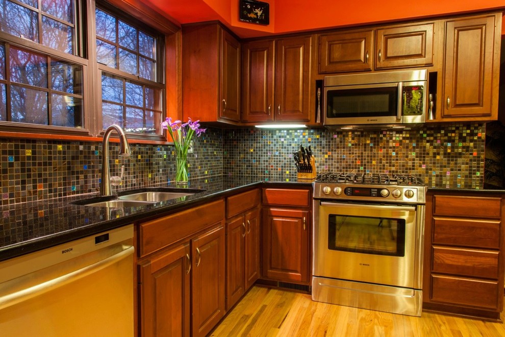 Exemple d'une grande cuisine américaine craftsman en L et bois brun avec un plan de travail en granite, une crédence multicolore, une crédence en carreau de verre, un électroménager en acier inoxydable et un sol en bois brun.