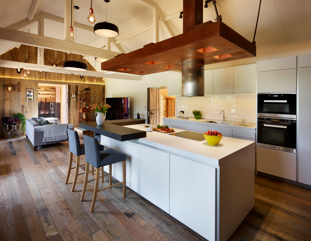 Mid-sized trendy single-wall medium tone wood floor eat-in kitchen photo in Wiltshire with flat-panel cabinets, white cabinets, laminate countertops, white backsplash, glass sheet backsplash, stainless steel appliances and an island