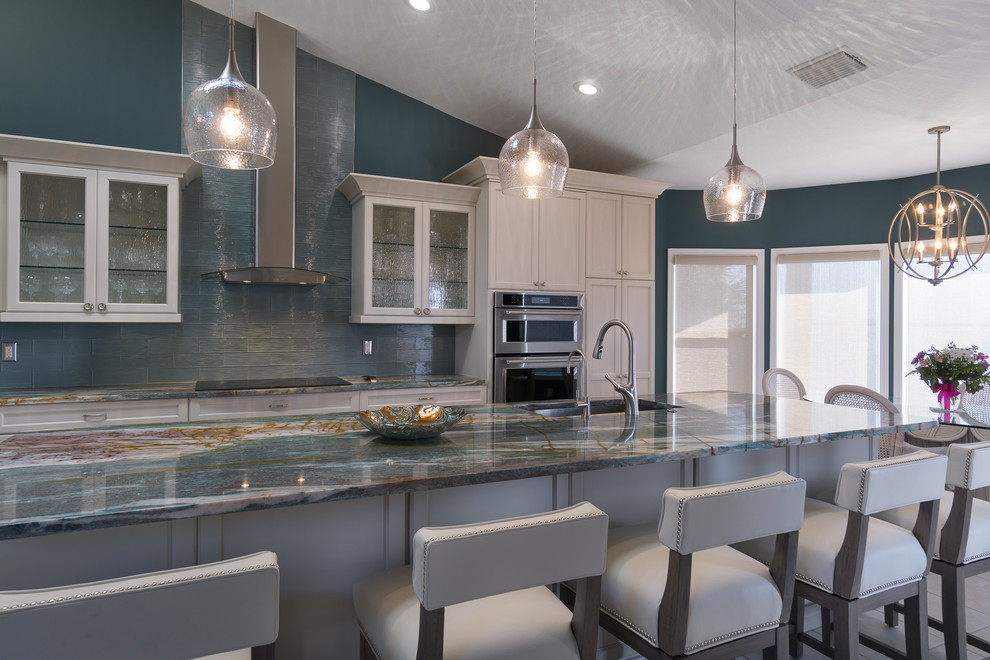 Mid-sized beach style l-shaped eat-in kitchen photo in Tampa with an undermount sink, recessed-panel cabinets, white cabinets, onyx countertops, blue backsplash, glass tile backsplash, stainless steel appliances and an island
